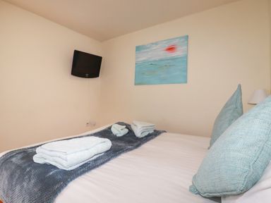A bedroom with a bed covered with a blanket and folded towels a wall-mounted TV and a painting at Oyster Atlantic Highway near Bude