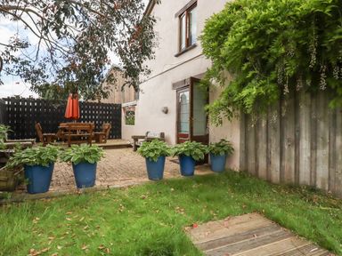 An outdoor area with green grass wooden decking potted plants a table with chairs and an umbrella by a building at Oyster Atlantic Highway near Bude