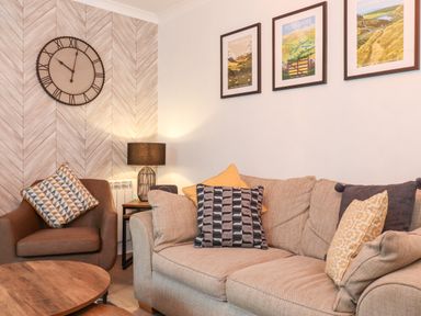 A sitting area with a beige sofa and brown armchair by a wooden coffee table and wall clock at Bluebell Hill in Bowness-On-Windermere