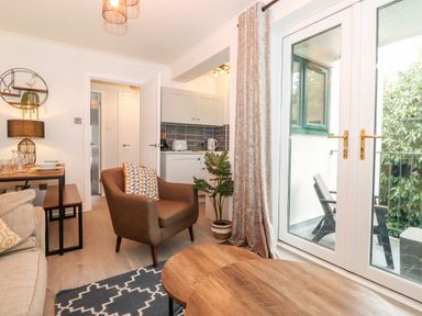 A living room with armchair coffee table and glass doors leading to a balcony at Bluebell Hill in Bowness-On-Windermere
