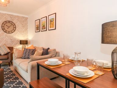 A dining table with plates glasses and a water jug next to a sofa with cushions and wall art at Bluebell Hill in Bowness-On-Windermere