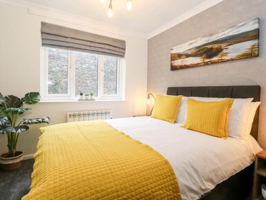 A bedroom with a bed with yellow pillows and blanket and a window with gray blinds at Bluebell Hill in Bowness-On-Windermere