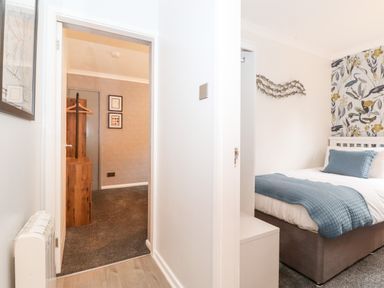 A hallway leading to a bedroom with a bed with blue bedding and a room with wooden furniture and framed pictures on the wall at Bluebell Hill in Bowness-On-Windermere