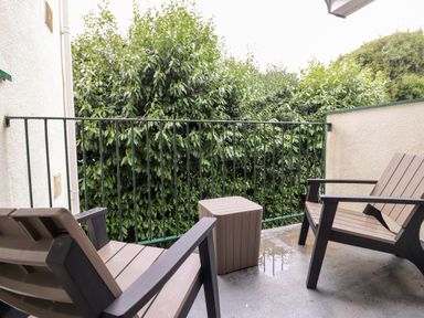 A balcony with two chairs and a small table overlooking green bushes at Bluebell Hill in Bowness-On-Windermere