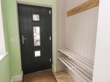 An entryway with a black door featuring three small windows a wooden coat rack with hooks and a white wooden bench at Landfall in St Twynnells near Pembroke