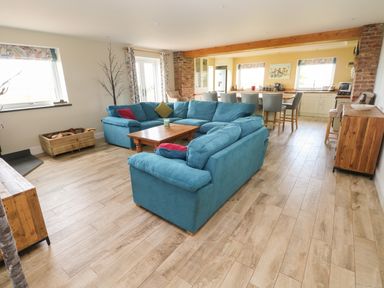 An open living room with blue sofas and a wooden coffee table connected to a kitchen with bar stools at Landfall in St Twynnells near Pembroke