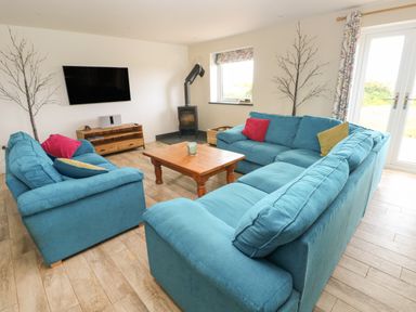 A living room with blue sofas a wooden coffee table a wall mounted TV and a wood burning stove at Landfall in St Twynnells near Pembroke