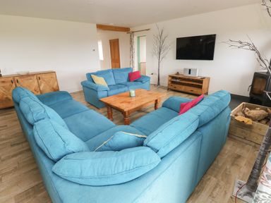 A living room with blue sofas wooden coffee table and cabinet with a wall mounted tv at Landfall in St Twynnells near Pembroke