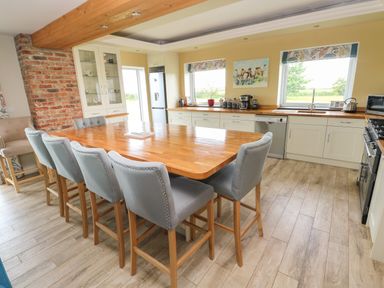 A kitchen with a large wooden table and six gray chairs near cabinets and windows at Landfall in St Twynnells near Pembroke