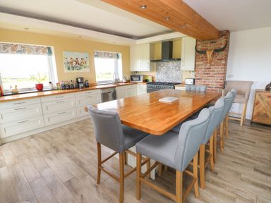 A kitchen with a wooden island and gray bar stools near windows and a brick chimney at Landfall in St Twynnells near Pembroke