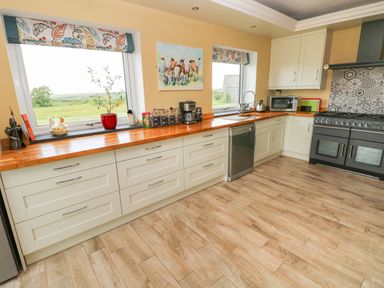 A kitchen with white cabinets wooden countertop two windows a dishwasher a stove and various kitchen items at Landfall in St Twynnells near Pembroke
