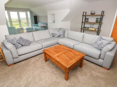 A living room with a gray sectional sofa and wooden coffee table at Landfall in St Twynnells near Pembroke