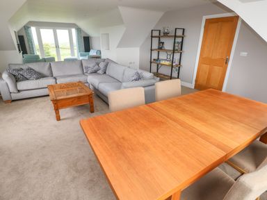 A living room with a gray corner sofa a wooden coffee table a dining table with chairs and a shelving unit at Landfall in St Twynnells near Pembroke