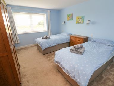 A bedroom with two single beds a wooden chest of drawers a window with white blinds and curtains at Landfall in St Twynnells near Pembroke
