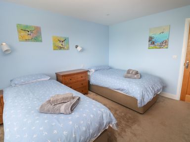 A bedroom with two single beds blue walls and bird paintings at Landfall in St Twynnells near Pembroke