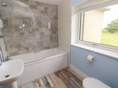 A bathroom with a bathtub shower combination a sink a toilet with toilet paper holder and a window with a view at Landfall in St Twynnells near Pembroke
