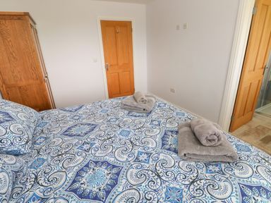 A bedroom with a bed covered in blue and white patterned bedding two wooden doors and a wooden wardrobe at Landfall in St Twynnells near Pembroke