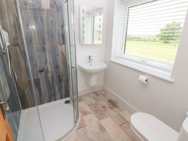 A bathroom with a curved glass shower enclosure a wall-mounted sink a toilet and a window with blinds at Landfall in St Twynnells near Pembroke