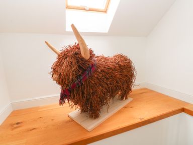 A wooden sculpture of a bull wearing a scarf on a wooden ledge in a room with white walls at Landfall in St Twynnells near Pembroke