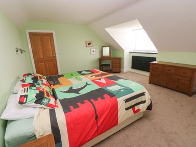 A bedroom with a bed with colorful bedding a wooden dresser a wooden vanity table with a mirror and a window with blinds at Landfall in St Twynnells near Pembroke