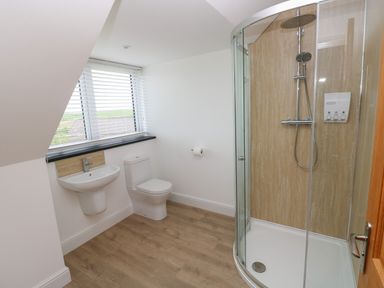 A bathroom with a corner shower enclosure a toilet a wall-mounted sink and a window with blinds at Landfall in St Twynnells near Pembroke