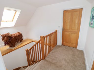 A carpeted stair landing with wooden railing a wooden door a skylight window and a decorative highland cow figure at Landfall in St Twynnells near Pembroke