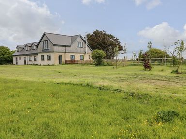 A large house with multiple windows and a fenced garden surrounded by grass and trees at Landfall in St Twynnells near Pembroke