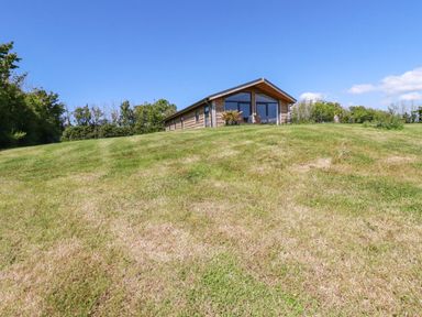 A wooden cottage on a grassy hill with trees in the background at Atlantic Lodge Atlantic Highway near Bude