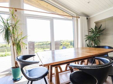 A dining area with a wooden table black chairs large windows and indoor plants at Atlantic Lodge Atlantic Highway near Bude
