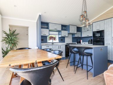 A kitchen with blue cabinets wooden dining table black chairs and pendant lights at Atlantic Lodge Atlantic Highway near Bude