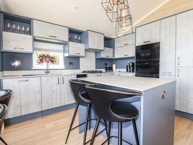 A kitchen with an island and three black bar stools at Atlantic Lodge Atlantic Highway near Bude