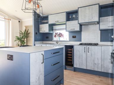 A kitchen with blue and wooden cabinets an island with drawers a gas stove and a window with plants at Atlantic Lodge Atlantic Highway near Bude