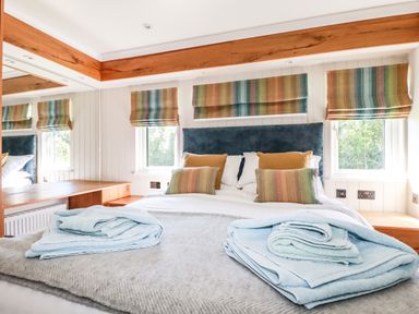 A bedroom with a bed and folded towels on it three windows with striped blinds and wooden desk at Atlantic Lodge Atlantic Highway near Bude