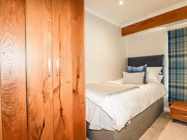A bedroom with a single bed with pillows and a blanket next to a wooden wardrobe and a bedside table with a drawer at Atlantic Lodge Atlantic Highway near Bude