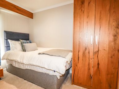 A bedroom with a single bed with pillows and a blanket and a wooden wardrobe at Atlantic Lodge Atlantic Highway near Bude