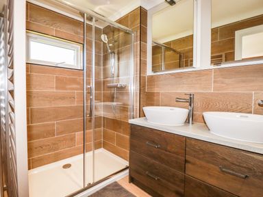 A bathroom with a glass shower enclosure and double sinks with wooden cabinets at Atlantic Lodge Atlantic Highway near Bude