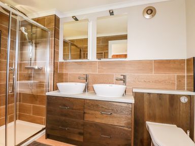 A bathroom with a glass shower enclosure double sinks with mirrors and a toilet at Atlantic Lodge Atlantic Highway near Bude