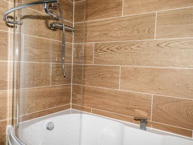 A bathtub with a showerhead and wood-patterned wall tiles at Atlantic Lodge Atlantic Highway near Bude