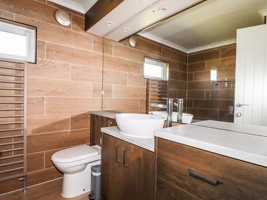 A bathroom with a toilet a sink with chrome faucet wooden cabinets large mirror and towel radiator at Atlantic Lodge Atlantic Highway near Bude