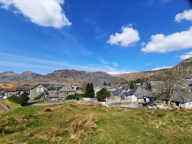 A village with stone houses and trees surrounded by mountains under a blue sky at Bridgeway House in Blaenau Ffestiniog