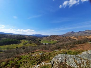A rural landscape with hills trees a road and mountains under a blue sky at Bridgeway House in Blaenau Ffestiniog