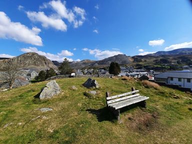 A bench on grassy hill overlooking a village with rocky hills and mountains in the background at Bridgeway House in Blaenau Ffestiniog