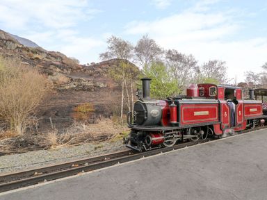 A red vintage steam train on railway tracks near dry vegetation and rocky hills at Bridgeway House in Blaenau Ffestiniog