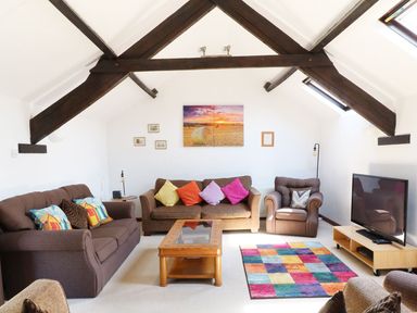 A sitting room with sofas colorful cushions a coffee table a multicolored rug a television and exposed wooden beams at The Corn Tallet in Westleigh near Bideford
