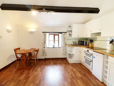 A kitchen with wooden flooring a dining table with chairs and white cabinets at The Corn Tallet in Westleigh near Bideford