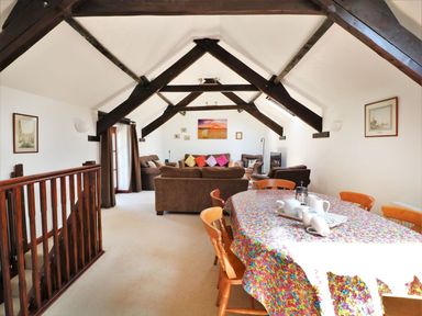An attic living room with exposed dark beams brown sofas colorful cushions a wooden dining table with chairs and a multicolored tablecloth at The Corn Tallet in Westleigh near Bideford
