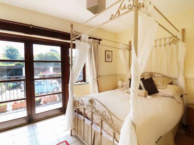 A bedroom with a canopy bed near large wooden framed glass doors and a window at The Corn Tallet in Westleigh near Bideford
