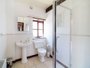 A bathroom with a pedestal sink, toilet, shower with glass door, window, and mirror at The Corn Tallet in Westleigh near Bideford