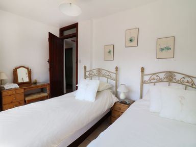 A bedroom with two single beds, bedside table with lamp, wooden dressing table with mirror, and three pictures on the wall at The Corn Tallet in Westleigh near Bideford