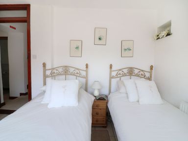 A bedroom with two single beds white bedding wooden nightstand with lamp and phone three framed pictures on wall at The Corn Tallet Westleigh near Bideford